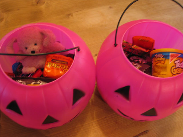 two pink plastic spherical buckets filled with Halloween candy